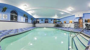 An indoor swimming pool with blue and white tiled walls, a clear pool, and lounge chairs along the sides.