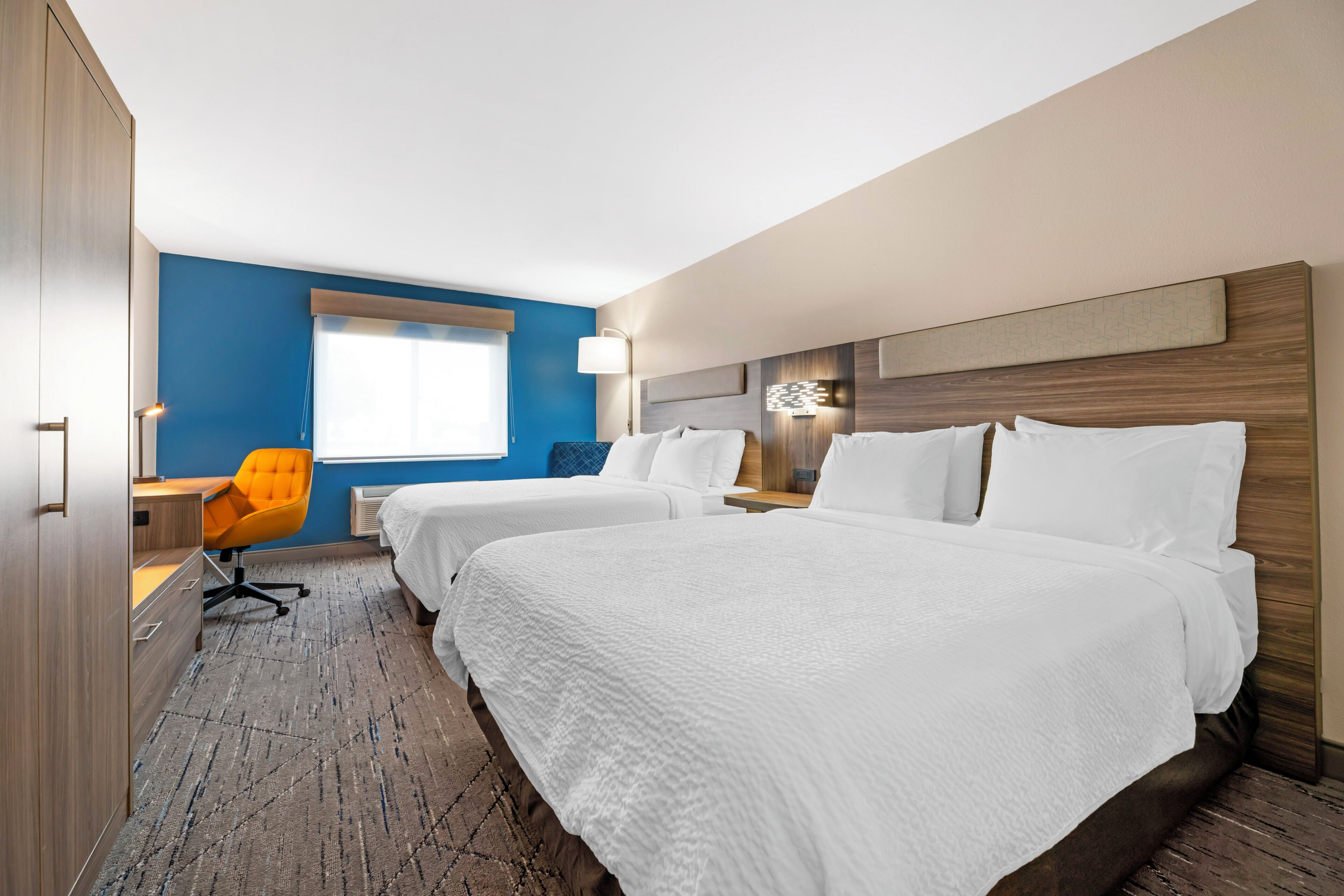 A hotel room with two beds, a desk, a chair, and a window with blinds.