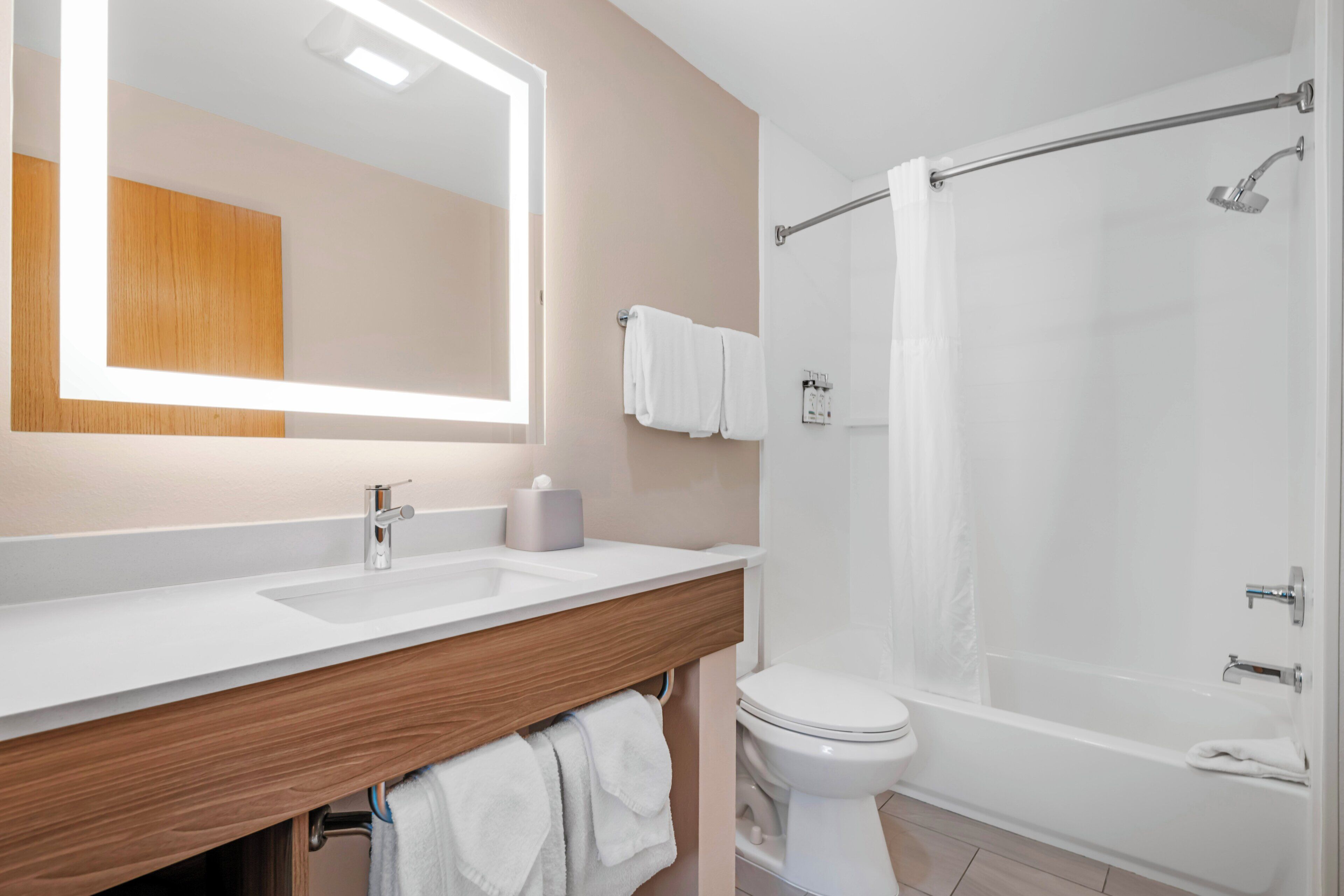 A bathroom with a large mirror, two sinks, a toilet, and a bathtub.