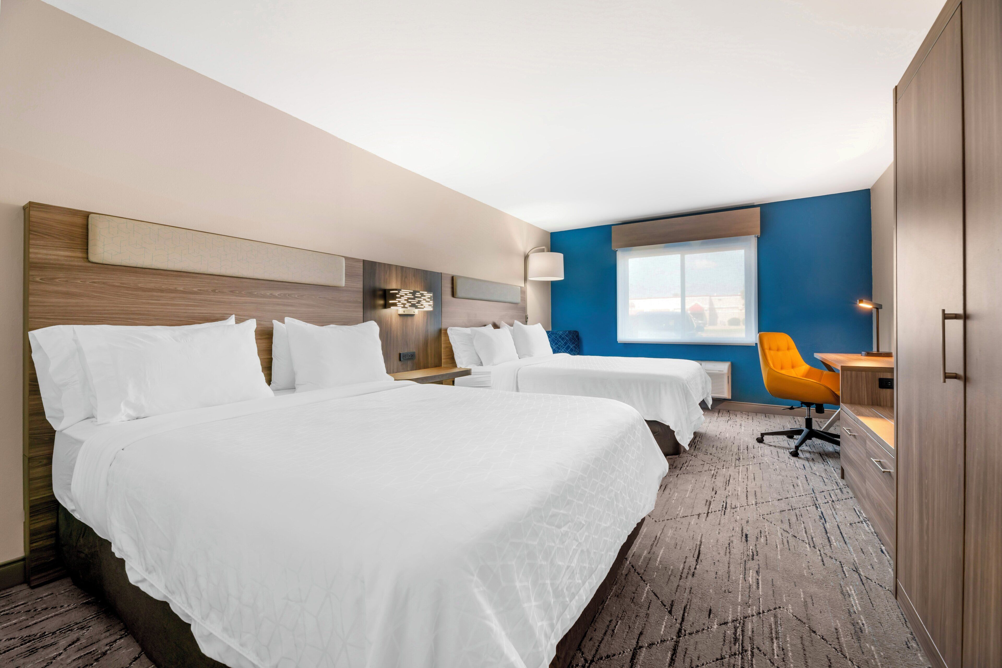 A hotel room with two beds, a desk, a chair, and a large window.