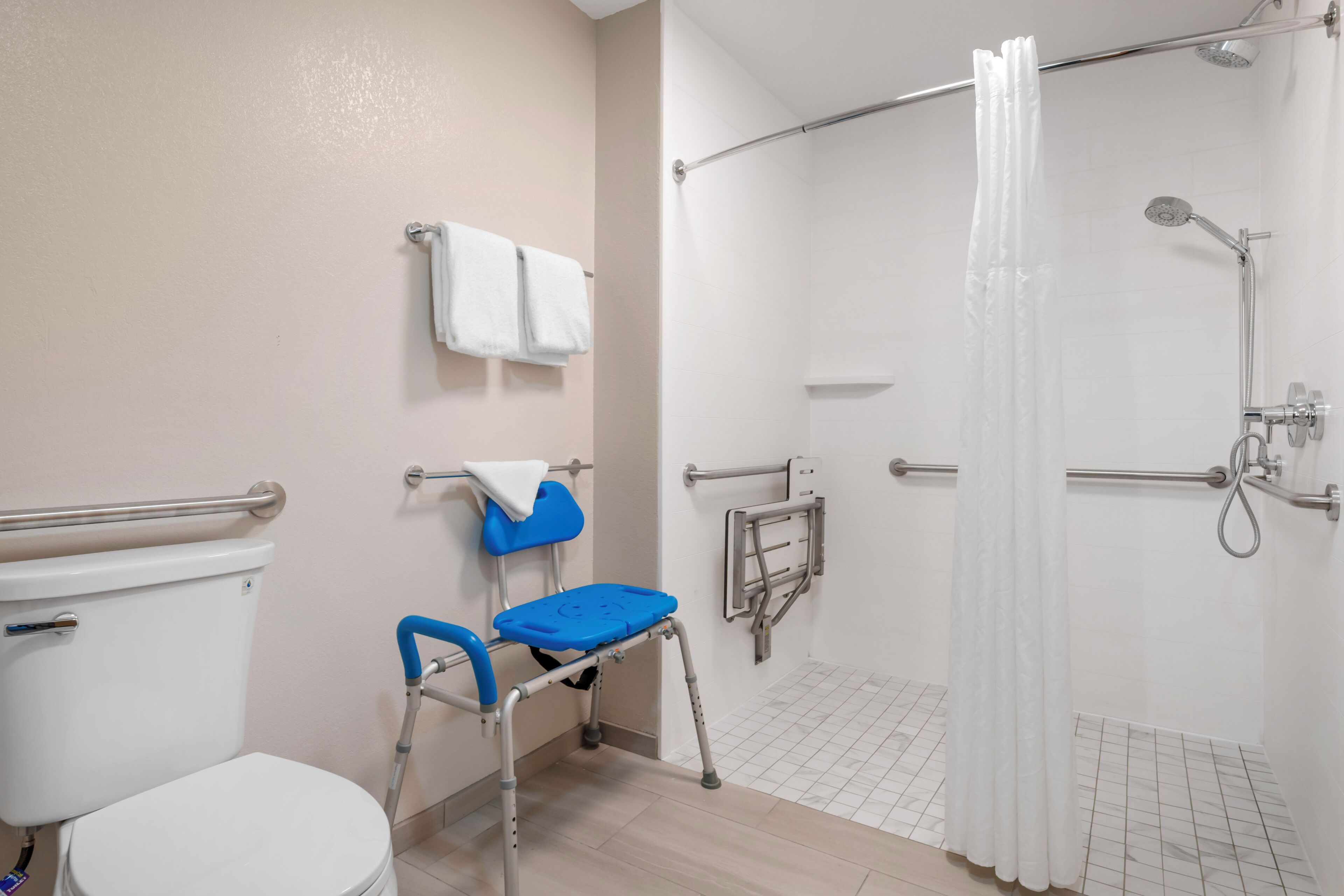 A bathroom with a toilet, a shower with a glass door, and a grab bar near the shower.