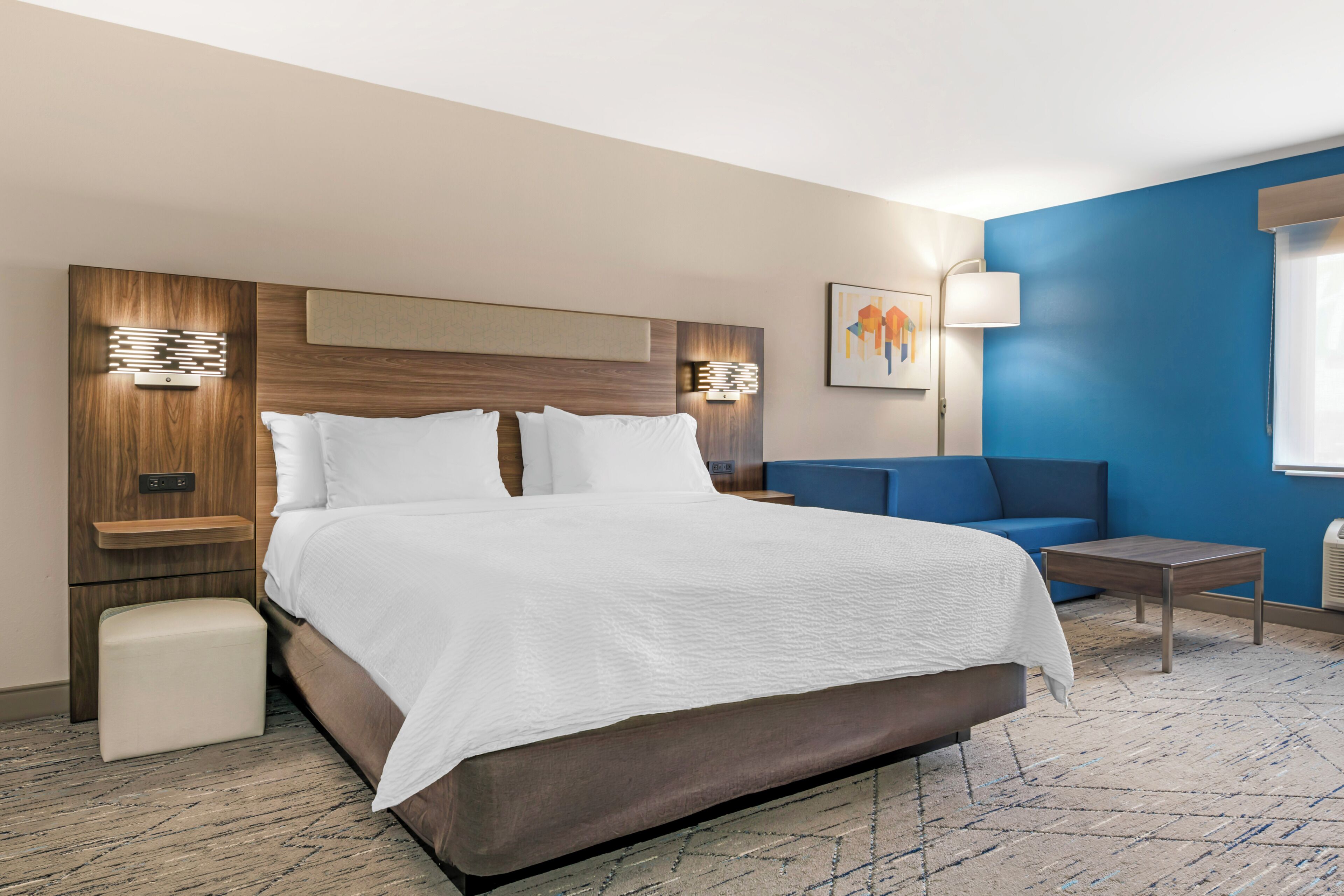 A hotel room with a large bed, bedside tables, a sofa, a lamp, and a painting on the wall.