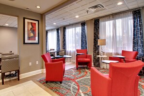 A hotel lobby with red chairs, a patterned carpet, and a framed picture on the wall.