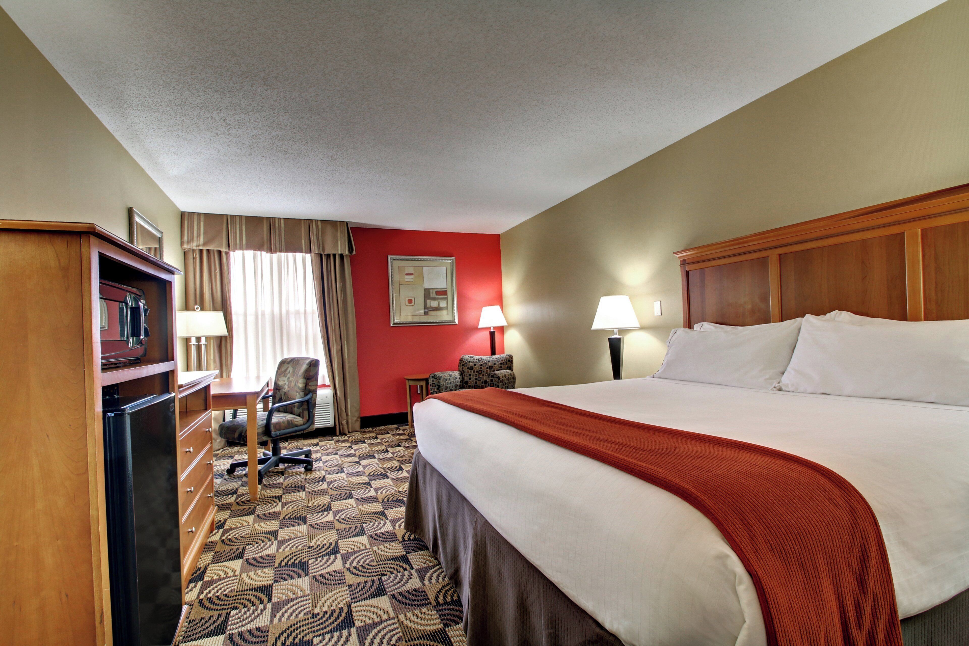 A hotel room with a bed, a desk, a chair, a television, and two lamps.