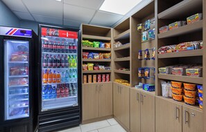 Un espace comprenant des distributeurs automatiques, avec un réfrigérateur rempli de produits Coca-Cola et un autre de bonbons Starburst, le tout entouré d’étagères garnies d’en-cas et de boissons.