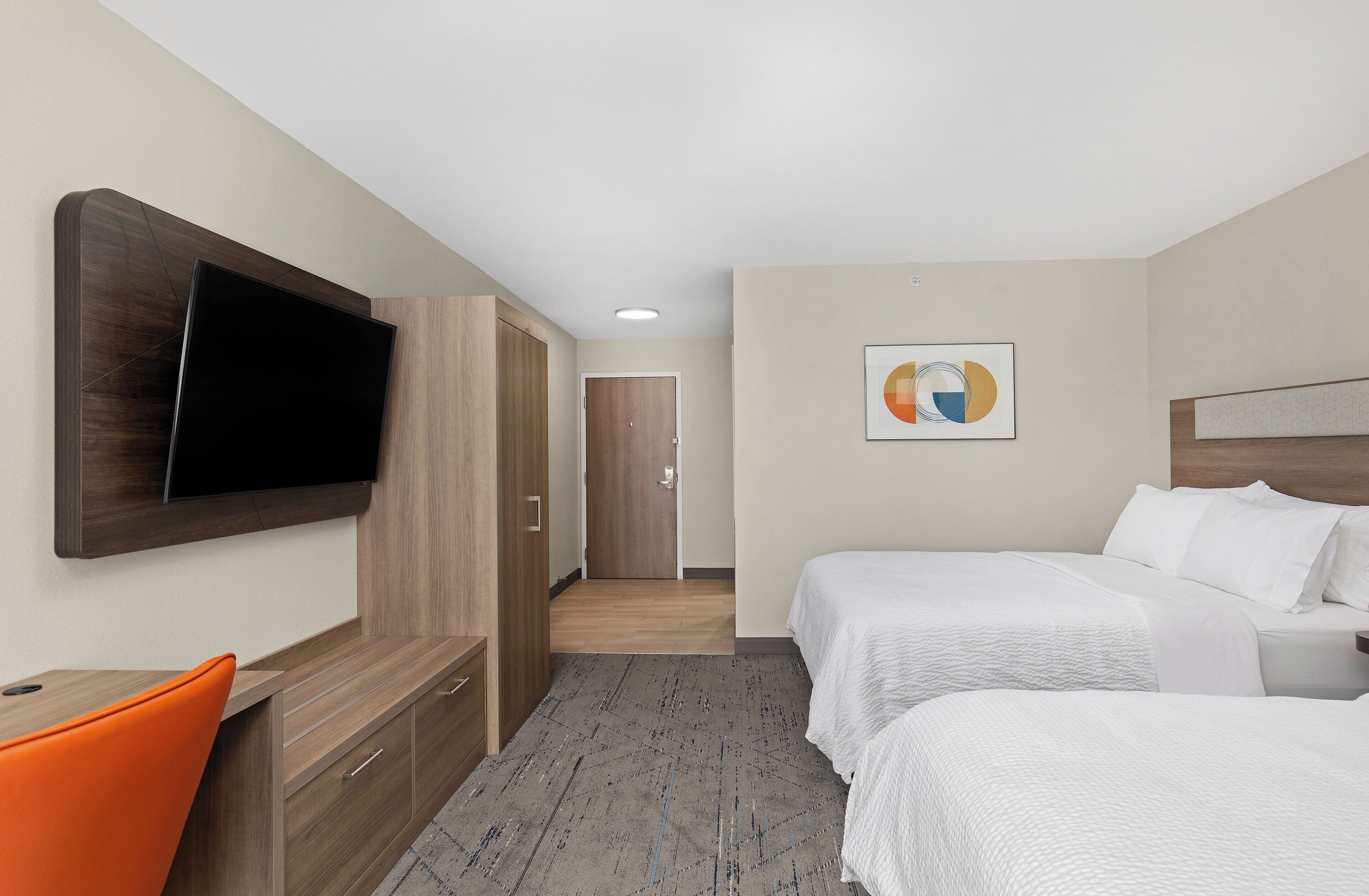 Habitació d'hotel amb dos llits, un televisor fixat a la paret, un armari de fusta i una porta que dona a una altra habitació.