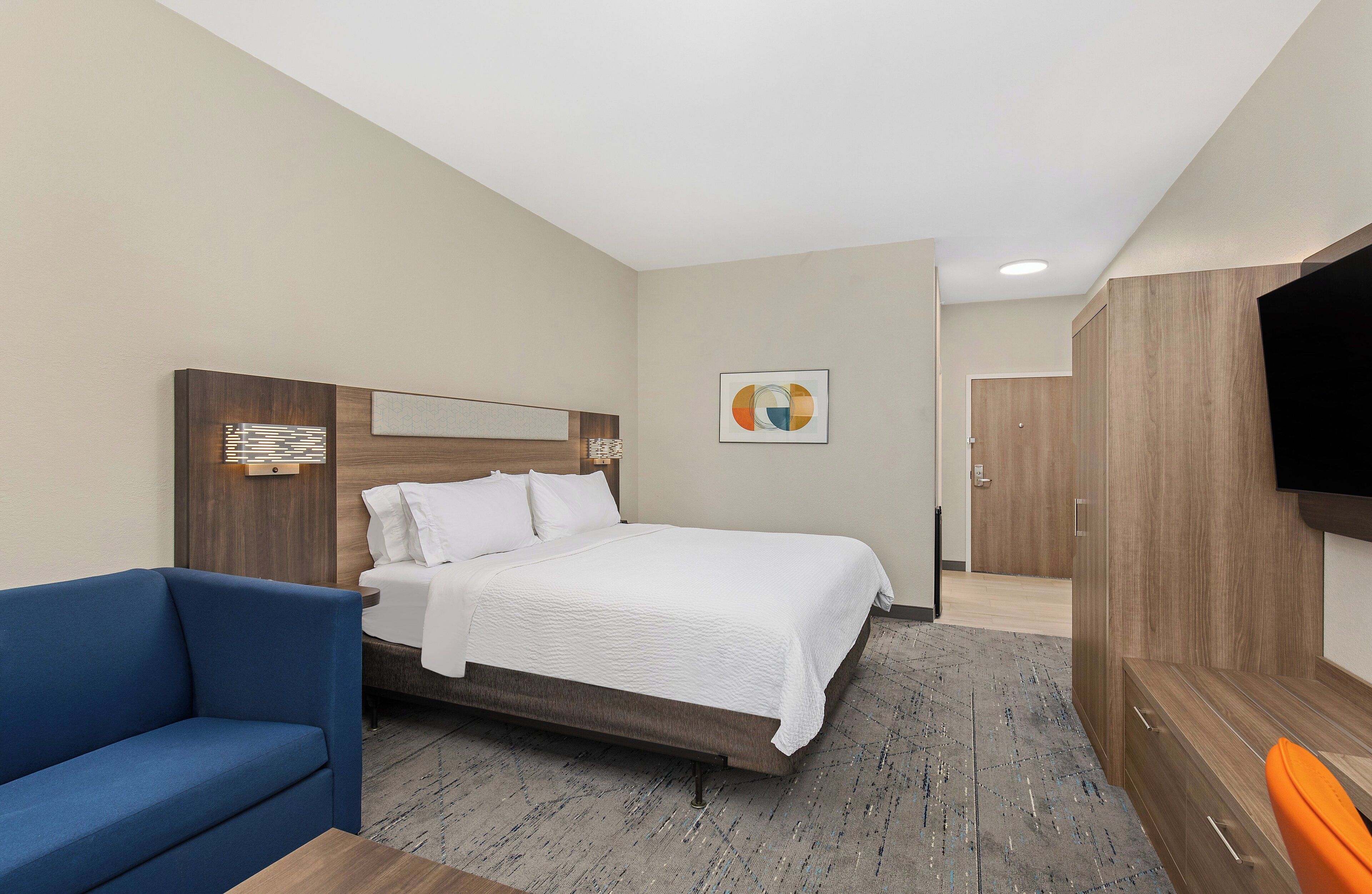 Une chambre d’hôtel avec un lit, un canapé bleu, une télévision et une armoire en bois.