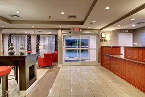 A hotel lobby with a reception desk, red seating area, and a view through the glass doors. - Holiday Inn Express Hurricane by IHG (Hurricane Mills)