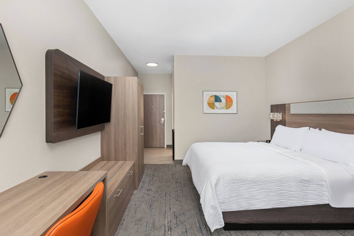 A hotel room with a bed, a desk, a chair, a TV, and a door leading to another room.