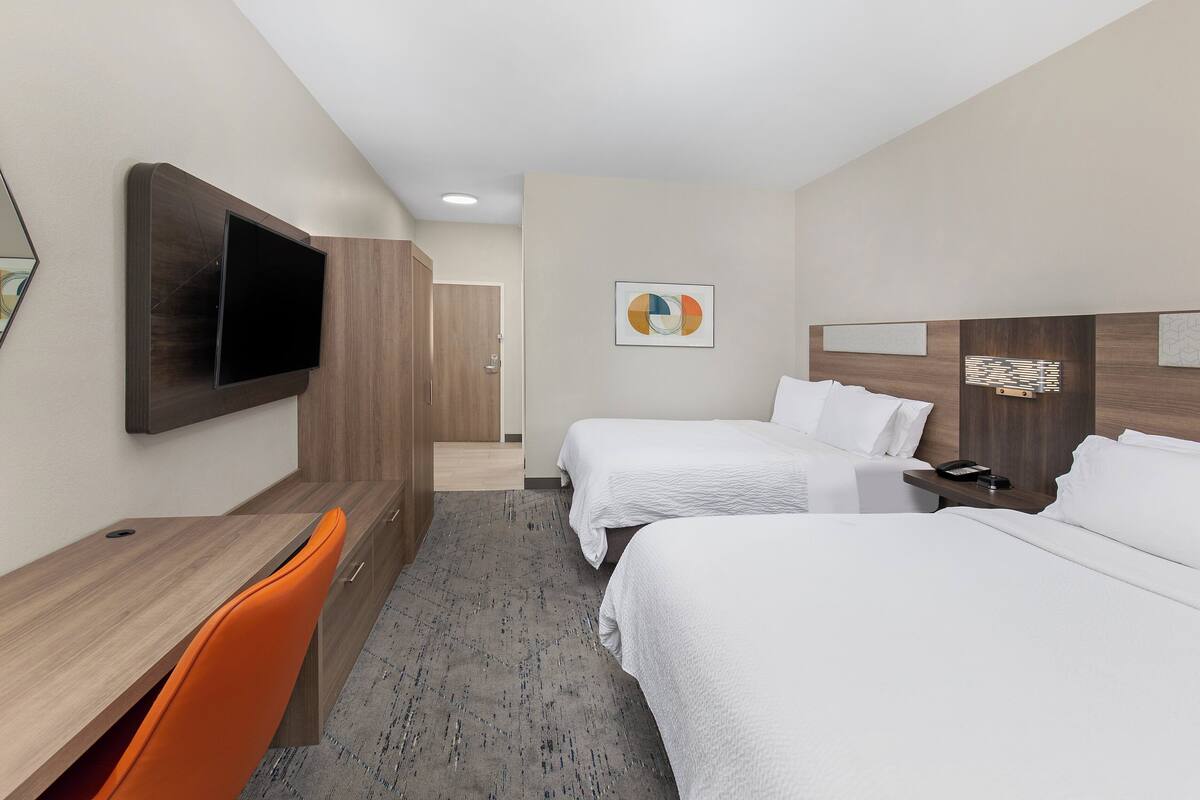 A hotel room with two beds, a desk, a chair, a TV, and artwork on the walls.