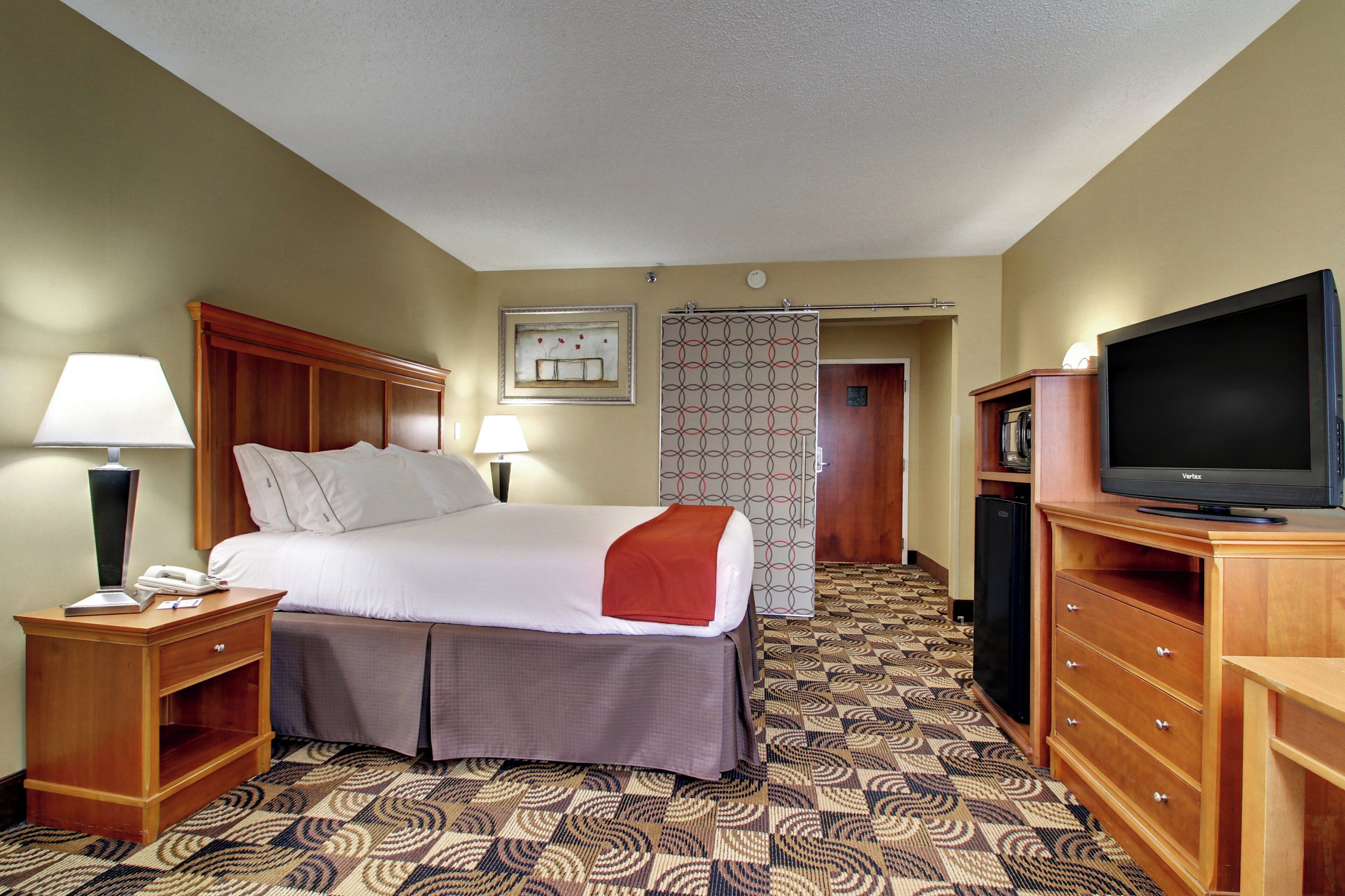 A hotel room with a bed, bedside lamps, a television, a desk with a telephone, and a patterned carpet.