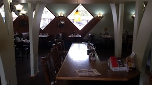 A restaurant with a long wooden table, multiple chairs, and a chandelier. There are two windows with light fixtures above them. - Hotel Blue Top Inn (Stevens Point)