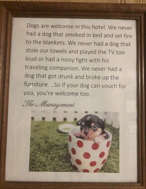 A framed sign with a humorous message about dogs and a picture of a puppy in a polka-dotted cup.