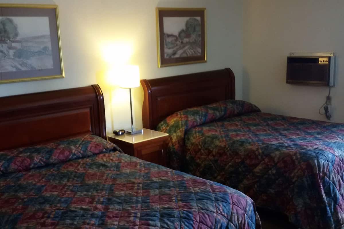 A hotel room with two beds, each with a patterned bedspread, a bedside table with a lamp, and two framed pictures on the wall.