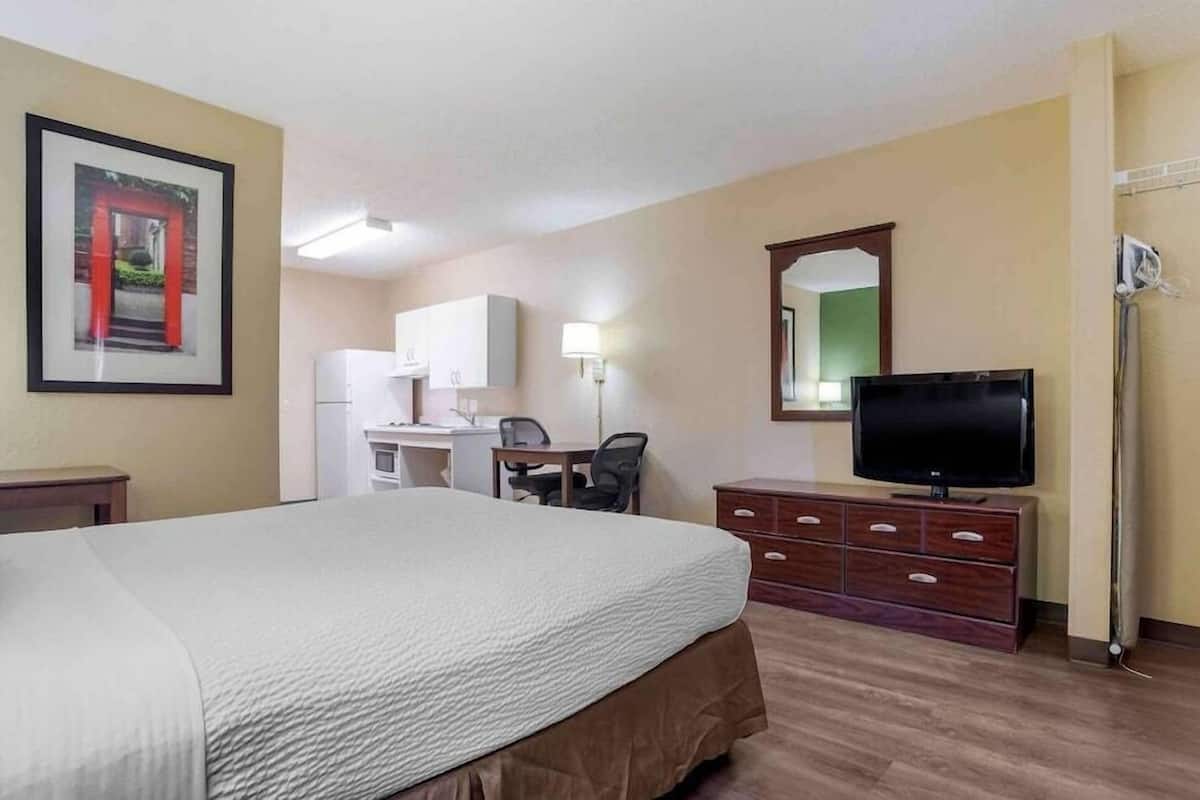 A hotel room with a bed, a desk with a chair, a television, and a mirror.