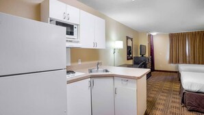 Quarto de hotel com cozinha compacta, uma cama, escrivaninha e espelho.