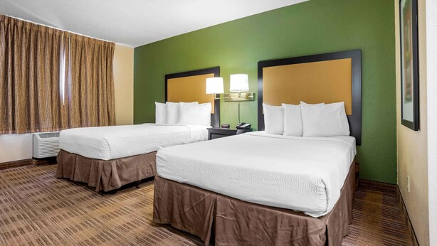 Quarto de hotel com duas camas, parede verde e janela com cortinas.