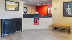 Un espace d’accueil d’hôtel avec un comptoir noir, une horloge, un banc et un mur d’accent rouge.