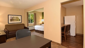 Une chambre d’hôtel équipée d’un lit, d’un bureau, d’une chaise, d’un réfrigérateur et d’une fenêtre avec des rideaux.
