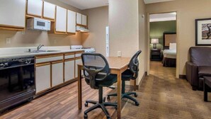 Une chambre d’hôtel compacte comprenant un coin cuisine, un espace repas avec deux chaises, un lit et un petit coin salon avec une chaise et une table.