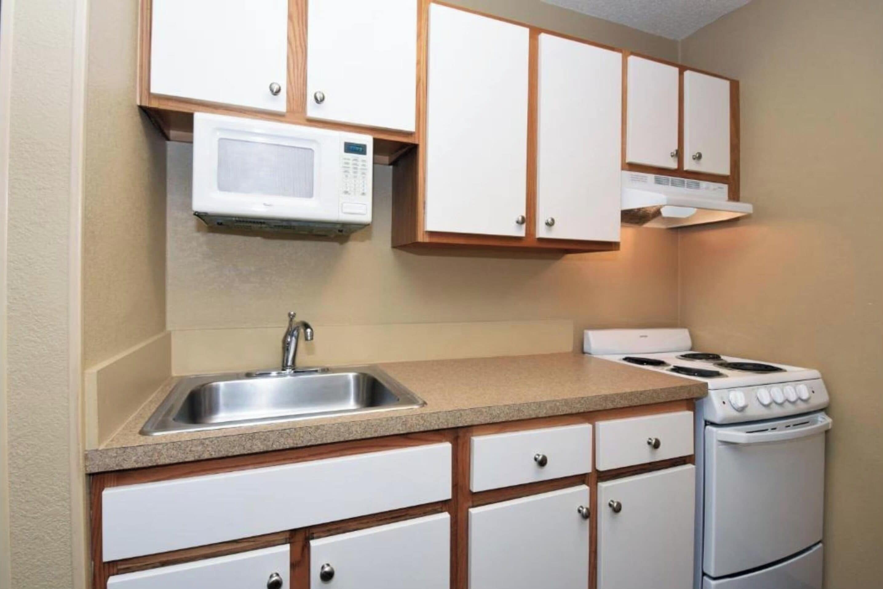 A kitchen with a microwave, stove, sink, and wooden cabinets.
