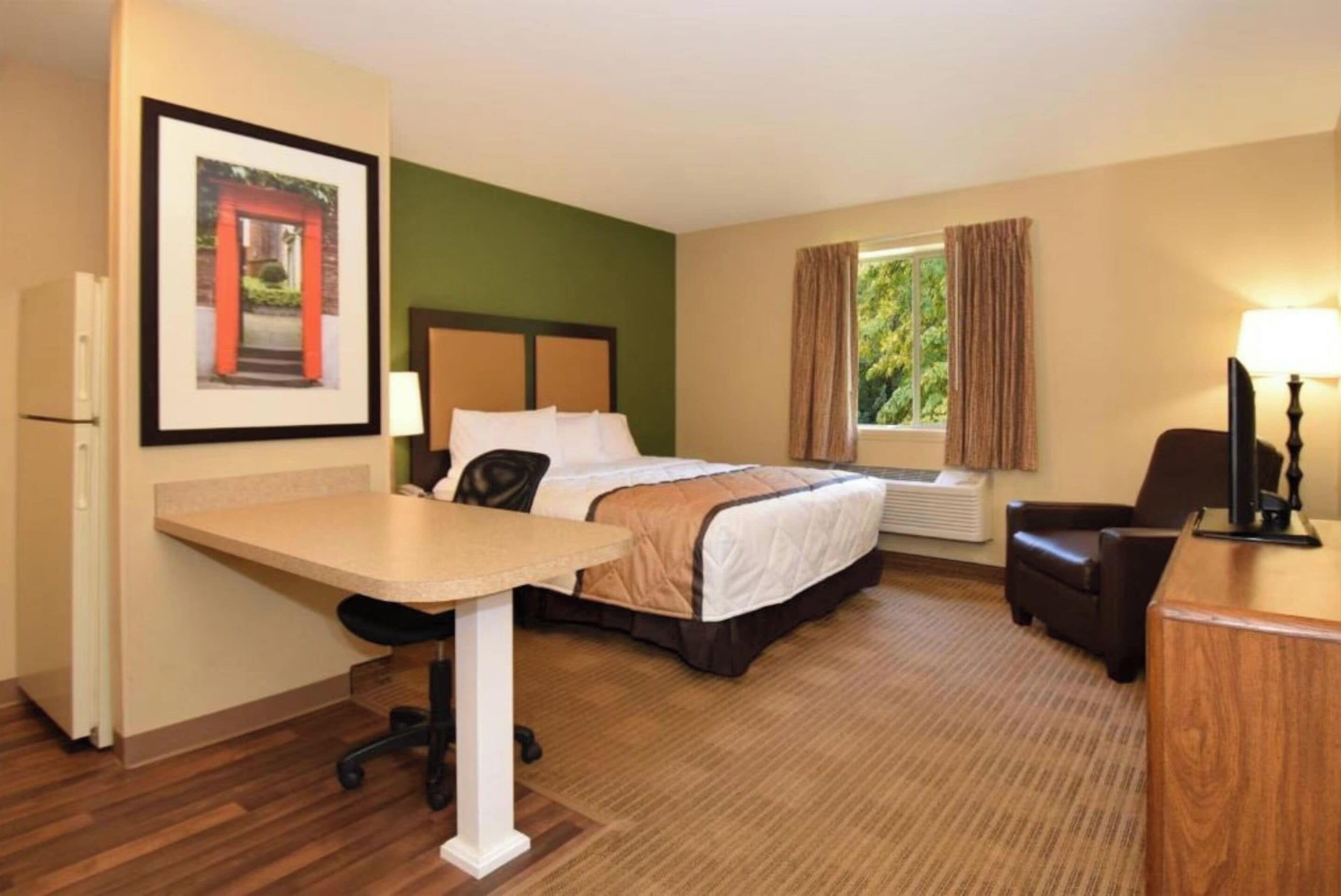 A hotel room with a bed, desk, chair, and a window with curtains.