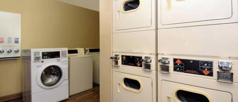 A laundry room with multiple washing machines and dryers, a whiteboard with information, and a wooden floor.