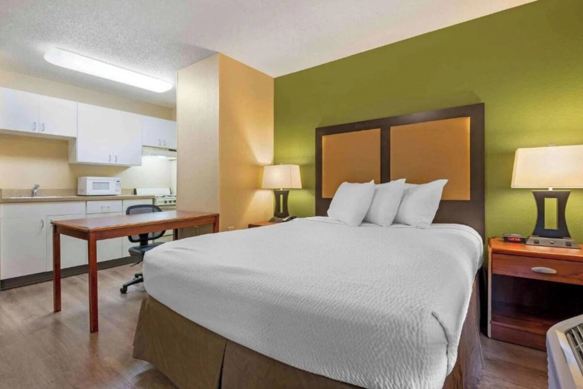 Ein Hotelzimmer mit einem Bett, Nachttischen, einem Schreibtisch, einer Mikrowelle und einer Küchenzeile.