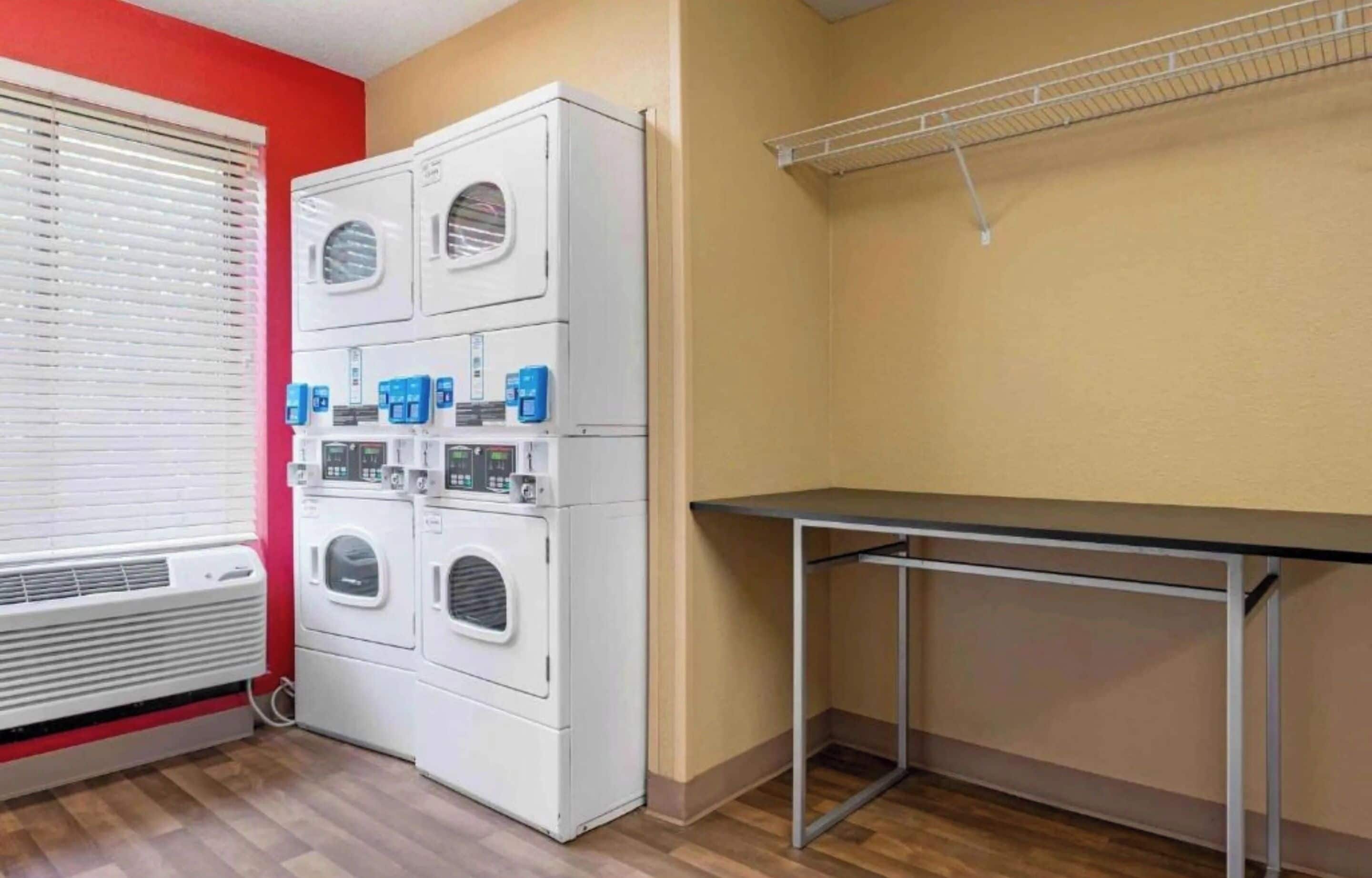 A laundry room with a stacked washer and dryer, a table, and a metal shelf.