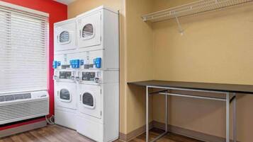 A laundry room with a stacked washer and dryer, a table, and a metal shelf.