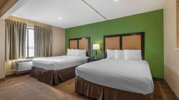 A hotel room with two beds, a window with curtains, a lamp, and a thermostat.