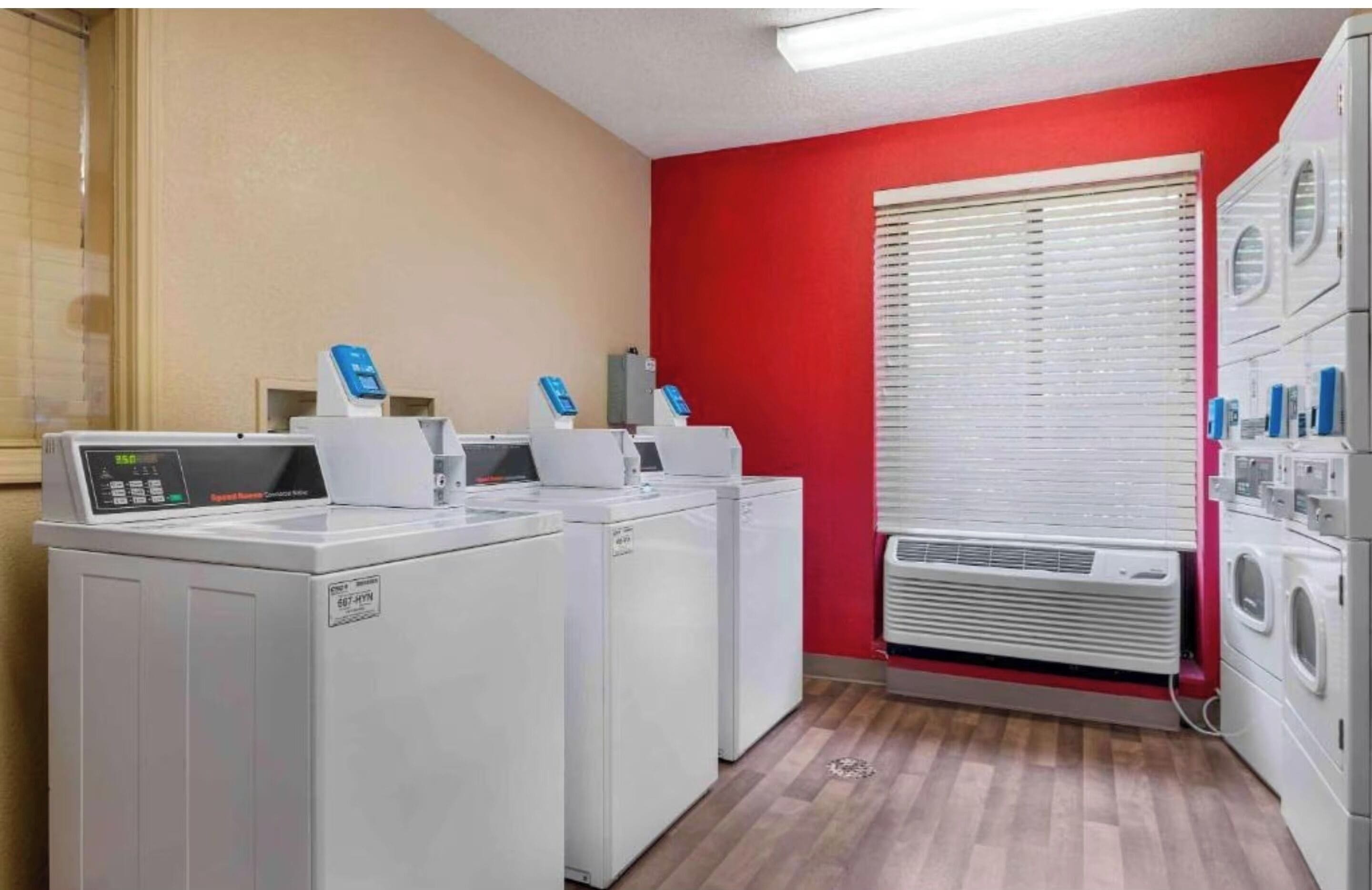 A laundry room with stacked washers and dryers, a control panel, and a window with blinds.