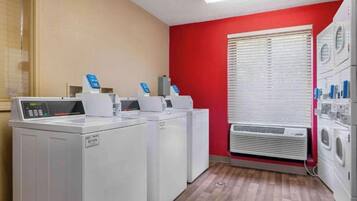 A laundry room with stacked washers and dryers, a control panel, and a window with blinds.