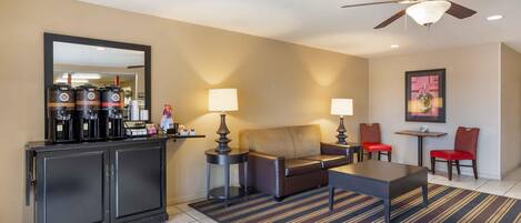 A hotel room with a sofa, a coffee station, a dining area with chairs, a table, and a ceiling fan.