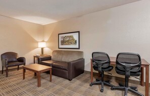 A hotel room with a sofa, two chairs, a desk, a lamp, and a framed picture on the wall.