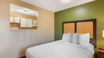 Quarto de hotel com cama, mesa de cabeceira, espelho e uma parede verde de destaque.