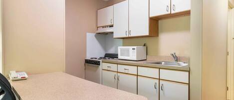 A compact kitchen with white cabinets, a microwave, a stove, and a sink.