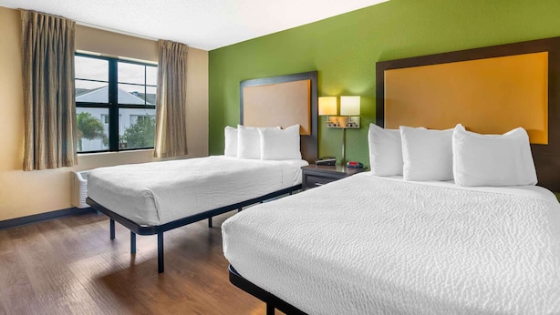 Une chambre d’hôtel avec deux lits, une grande fenêtre avec des rideaux, une table de chevet avec une lampe et un mur vert.