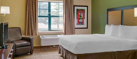 Een hotelkamer met een groot bed, een bureau met stoel, een raam met gordijnen en een ingelijst schilderij aan de muur.