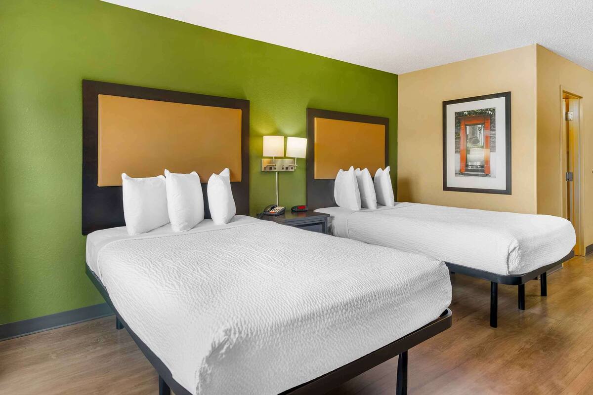 Une chambre d’hôtel avec deux lits, des murs verts, un tableau encadré et une lampe de chevet.