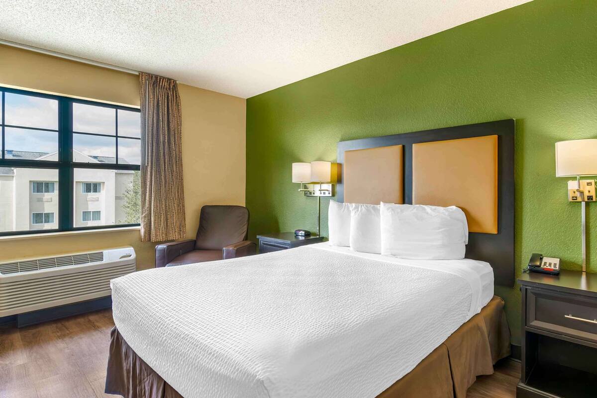 Une chambre d’hôtel avec un grand lit, une chaise, un bureau et une fenêtre avec des rideaux.