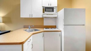 Une cuisine de taille réduite, avec des meubles blancs, un four à micro-ondes, une cuisinière et un réfrigérateur.