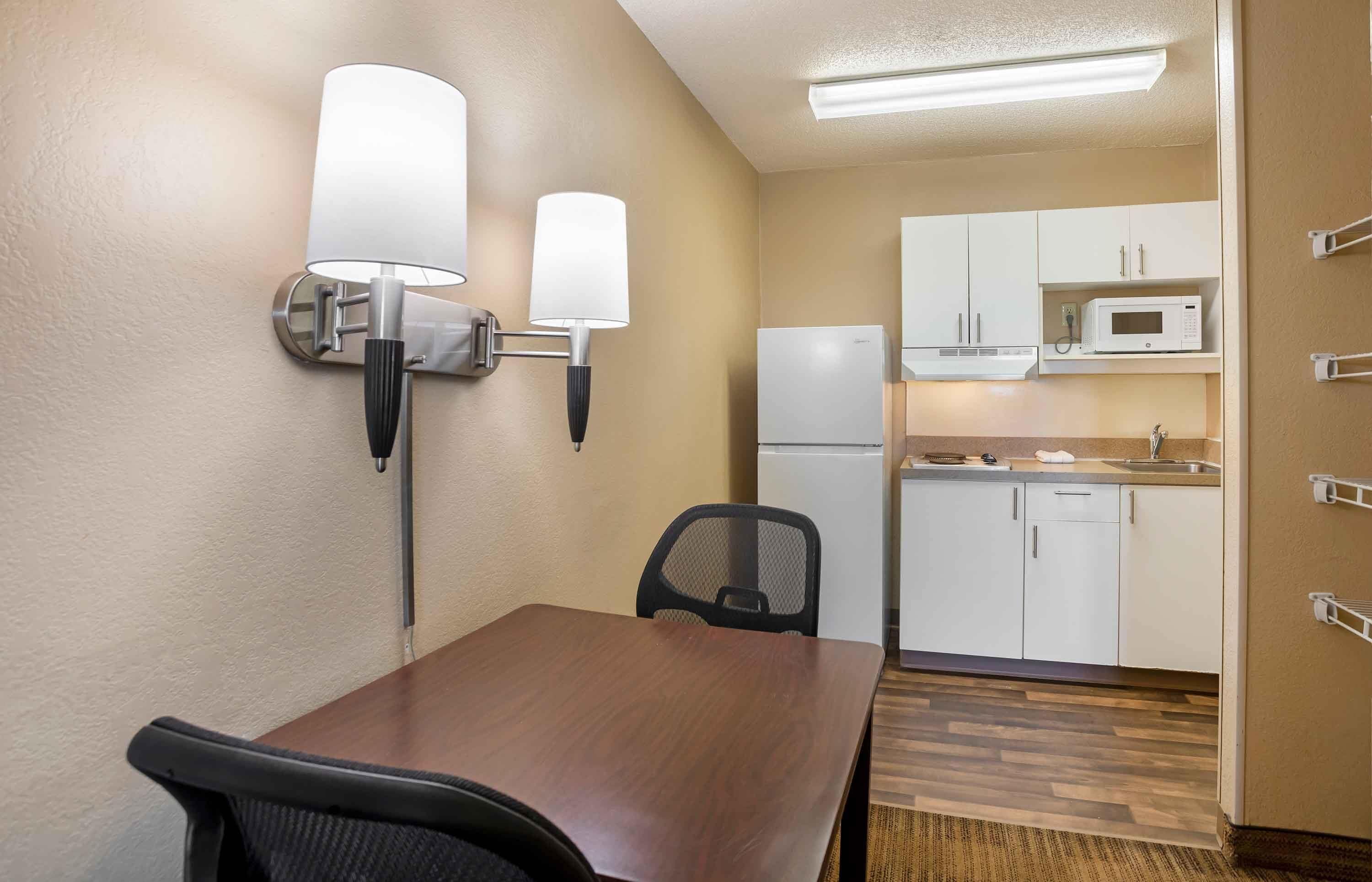 Una pequeña kitchenette con microondas, refrigerador y lavamanos. Hay un comedor con mesa y sillas, y lámparas fijadas a la pared.