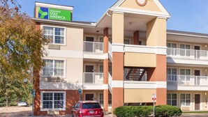 A multi-story hotel with a sign for Extended Stay America, balconies, and a parking area. - Extended Stay America Select Suites Raleigh RDU Airport (Morrisville)