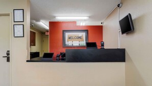 A reception desk with a 'WELCOME' sign, a flat-screen TV, and a security camera. - Extended Stay America Select Suites Raleigh RDU Airport (Morrisville)