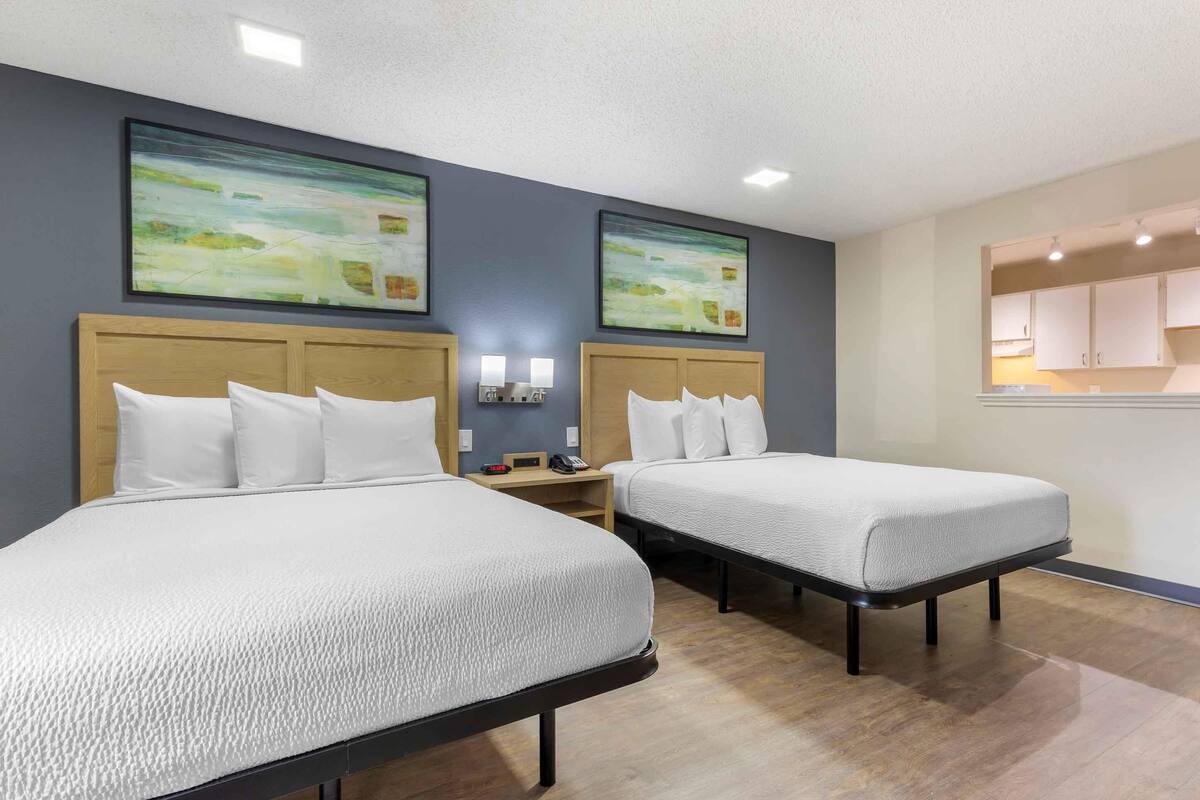 A hotel room with two beds, a nightstand, and a wall-mounted shelf.