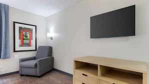 A room with a grey armchair, a wooden TV stand, and a framed picture on the wall. - Extended Stay America Suites Arlington Six Flags (Arlington)