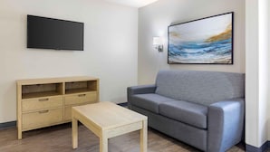 A modern living room with a grey sofa, a wooden TV stand, a small table, and a painting on the wall. - Extended Stay America Suites Arlington Six Flags (Arlington)