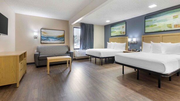 A hotel room with a sofa, two single beds, a wooden desk, and artwork on the walls. - Extended Stay America Suites Arlington Six Flags (Arlington)
