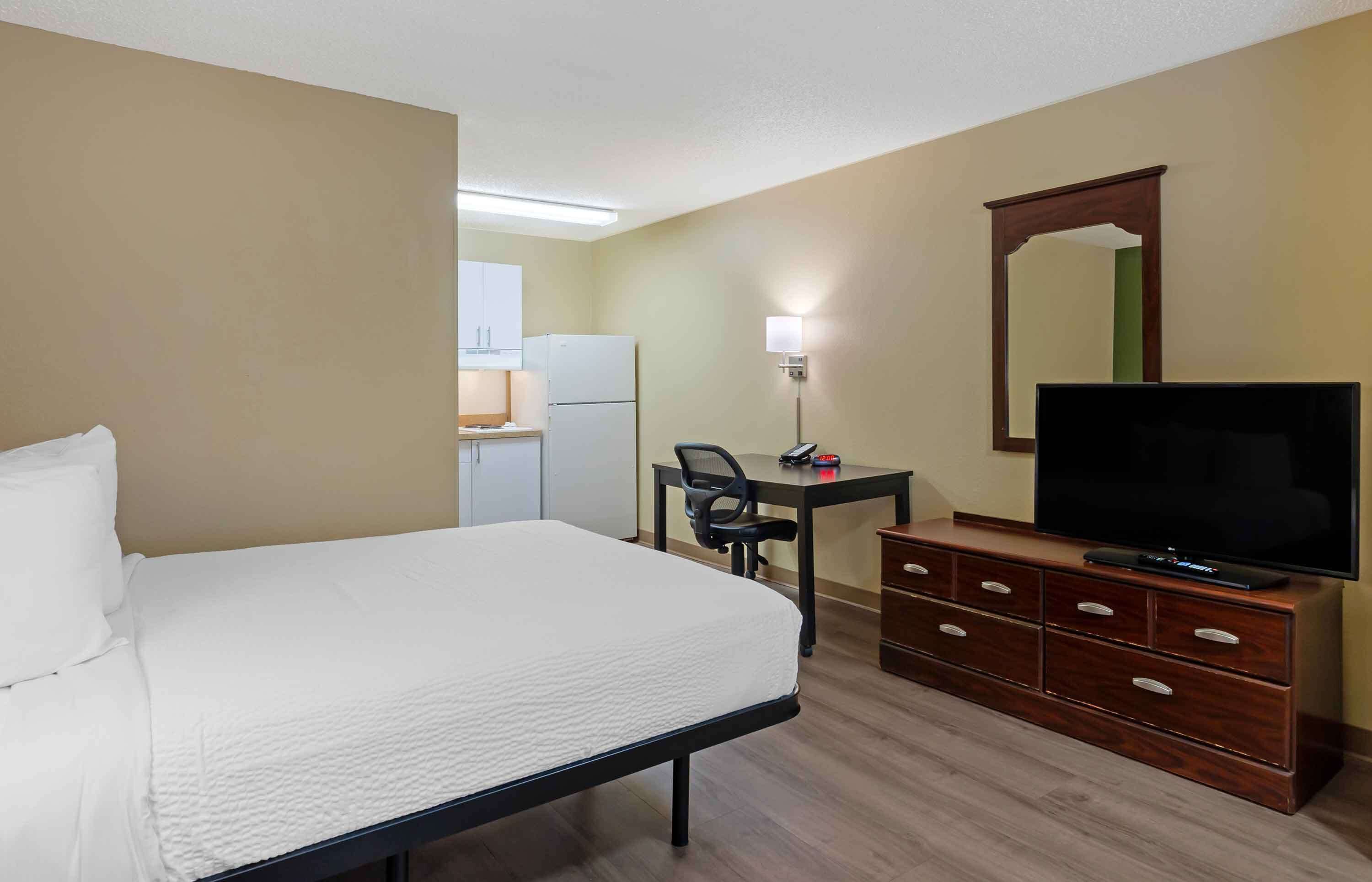 A hotel room with a bed, a desk with a chair, a television on a dresser, and a mirror on the wall.